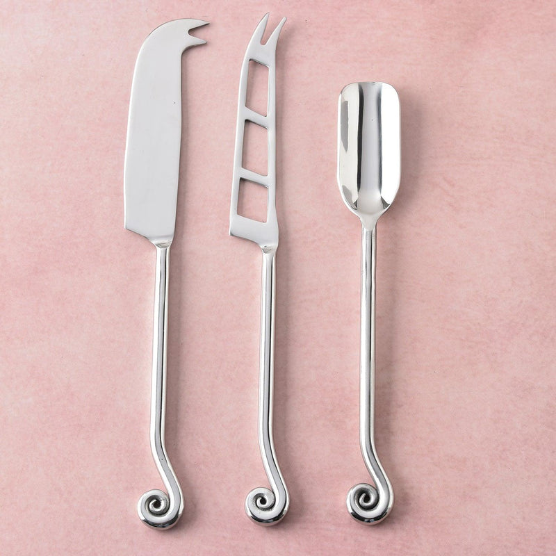 Three elegant cheese tools with spiral handles on a soft pink background. 